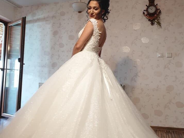 Rochie de mireasă tip prințesă cu plasă și mâneci pe umăr, decolteu adânc, îmbrăcată în dantelă aplicată manual și fustă amplă din tulle cu surje