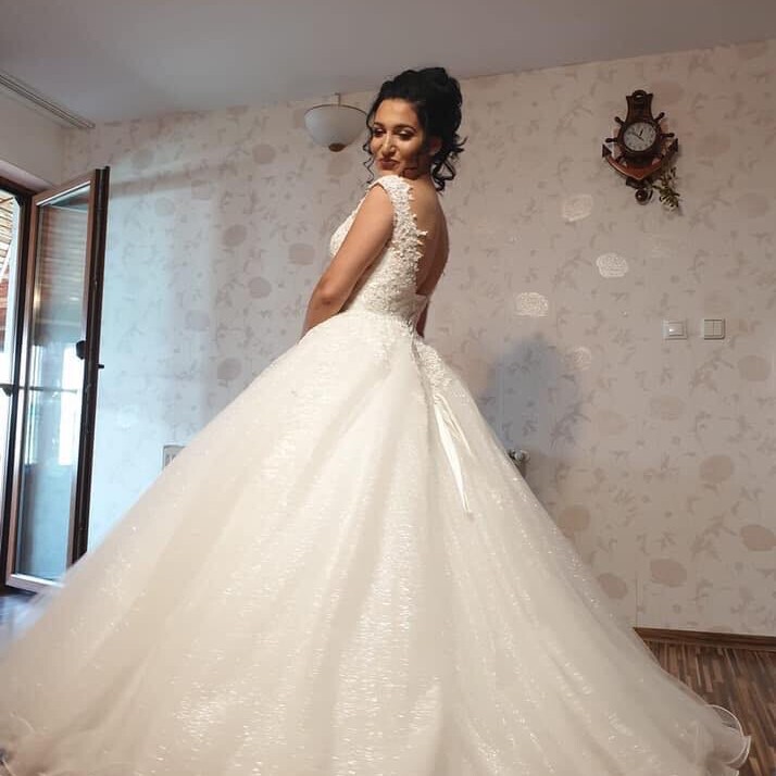 Rochie de mireasă tip prințesă cu plasă și m&acirc;neci pe umăr, decolteu ad&acirc;nc, &icirc;mbrăcată &icirc;n dantelă aplicată manual și fustă amplă din tulle cu surje